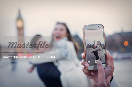 Personal perspective, playful couple hugging and being photographed with camera phone near Big Ben, London, UK