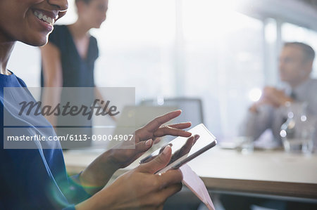 Close up smiling businesswoman using digital tablet in conference room meeting