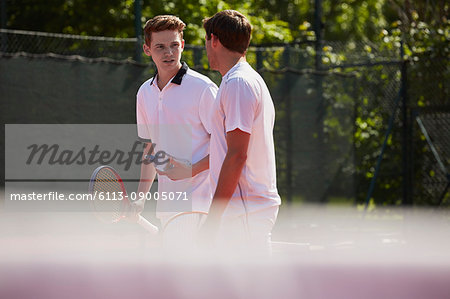 Male tennis players with tennis rackets talking on sunny tennis court