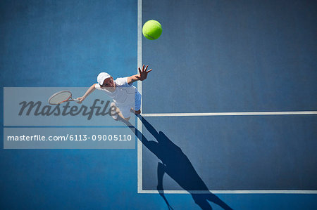 Overhead view of young male tennis player playing tennis, serving the ball on sunny blue tennis court Overhead view of young male tennis player playing tennis, serving the ball on sunny blue tennis court