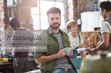 Portrait confident young male designer drinking coffee in workshop