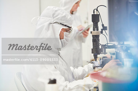 Workers in protective suits using machinery in fiber optics research and testing laboratory