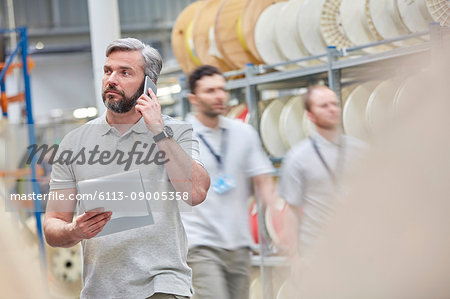 Male supervisor with clipboard talking on ell phone in fiber optics factory
