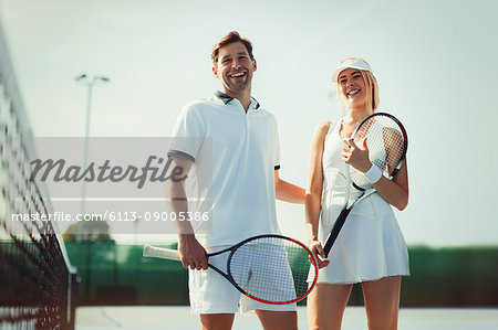 Portrait smiling, confident tennis players holding tennis rackets on sunny tennis court