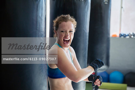 Portrait exuberant female boxer screaming, wrapping wrists in gym