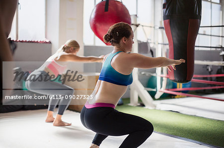 Young women doing squats next to boxing ring in gym