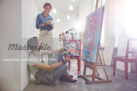 Artists drinking coffee painting at easel in art class studio