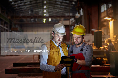 Male foreman and engineer using digital tablet in dark factory Male foreman and engineer using digital tablet in dark factory