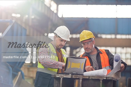 Male foreman and engineer working at laptop with blueprints in factory