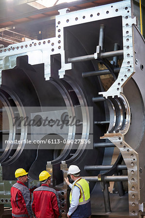 Male workers examining large steel equipment in factory