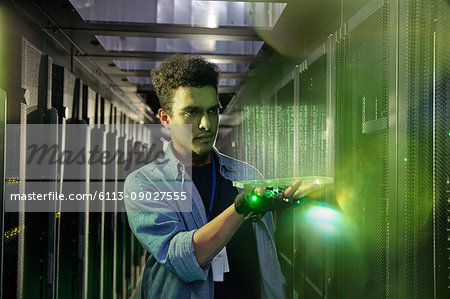 Male IT technician holding glowing futuristic digital tablet in server room Male IT technician holding glowing futuristic digital tablet in server room