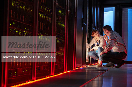 IT technicians talking at glowing panel in dark server room