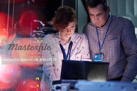IT technicians working at laptop in dark server room