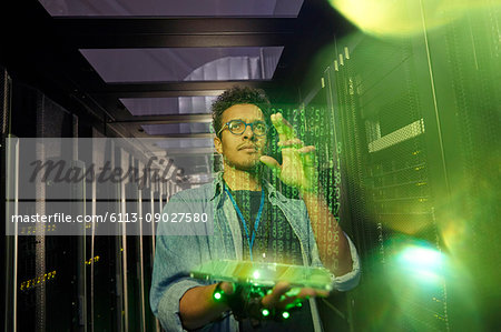 Male IT technician using futuristic digital tablet in dark server room