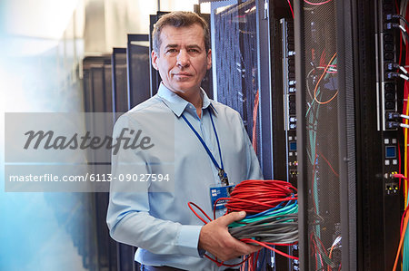 Portrait serious male IT technician holding cables in server room