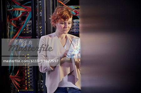 Female IT technician using futuristic digital tablet in server room Female IT technician using futuristic digital tablet in server room