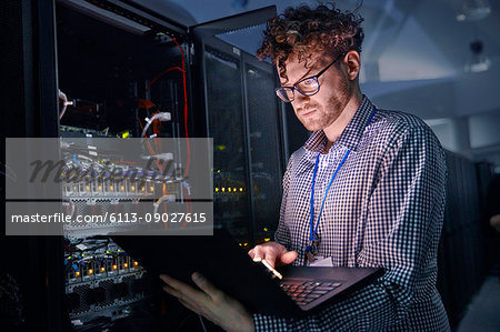 Focused male IT technician working at laptop in dark server room Focused male IT technician working at laptop in dark server room