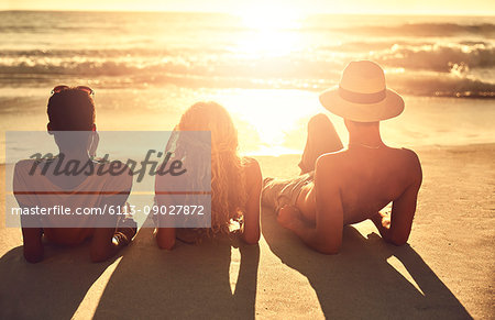 Carefree young friends relaxing on sunny summer sunset ocean beach