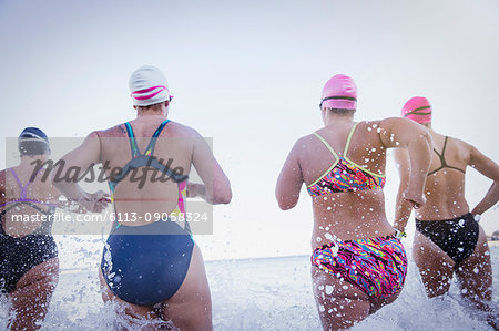 Female open water swimmers running and splashing in ocean surf