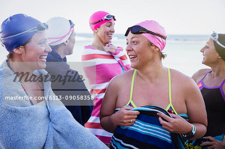 Female open water swimmers talking and drying off with towels on beach