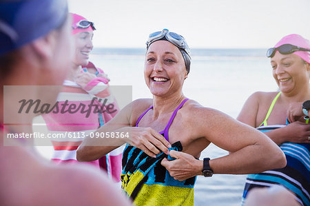 Smiling female open water swimmers drying off with towels on beach Smiling female open water swimmers drying off with towels on beach