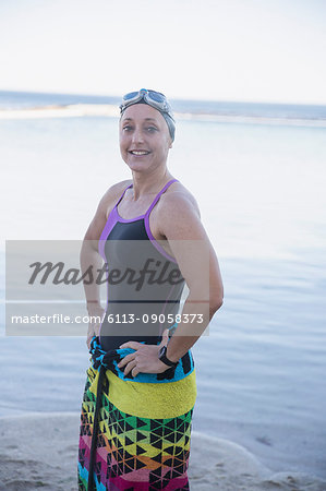 Portrait smiling, confident female open water swimmer wrapped in towel on ocean beach