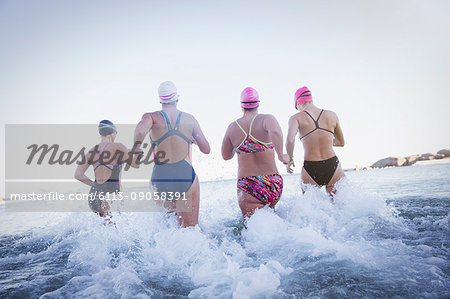 Female open water swimmers running and splashing in ocean surf