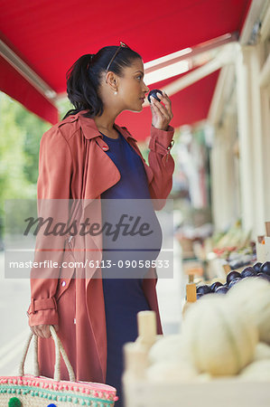 Pregnant woman shopping, smelling fruit at market storefront