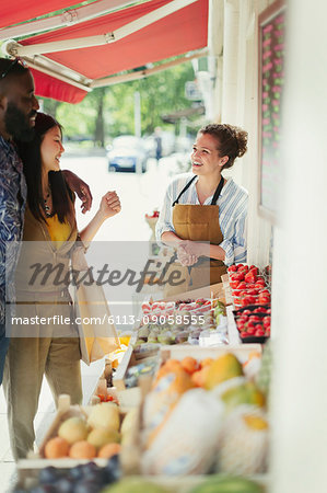 Female worker helping young couple shopping for fruit at market storefront