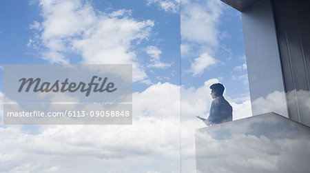 Pensive businessman standing on modern balcony looking at blue sky and clouds
