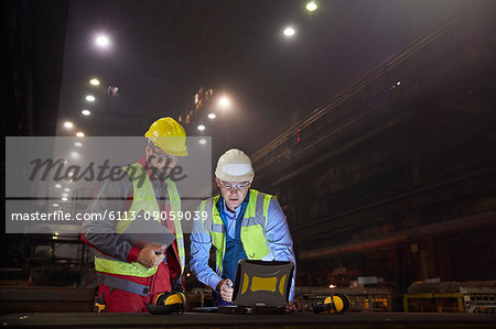 Steelworkers using laptop in dark steel mill