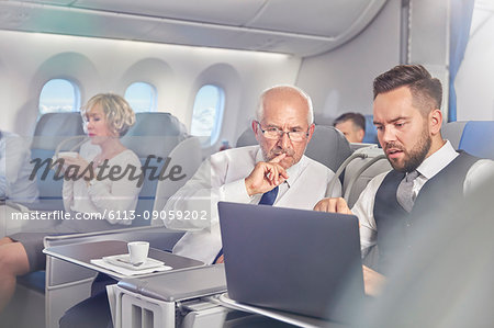 Businessmen working at laptop in first class on airplane