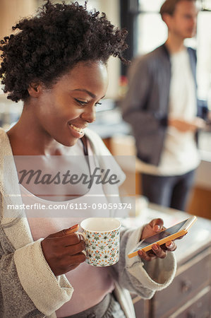 Smiling woman drinking coffee, texting with smart phone
