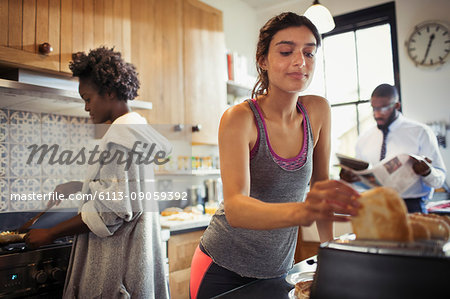 Woman toasting bread in toaster in kitchen