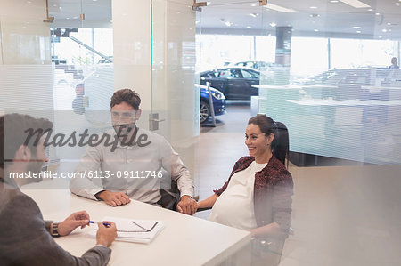 Car salesman talking to pregnant couple in car dealership office