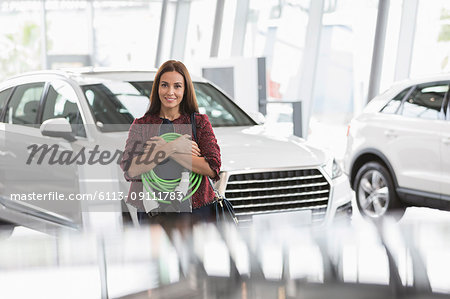 Portrait smiling female customer holding hybrid charging cable in car dealership showroom