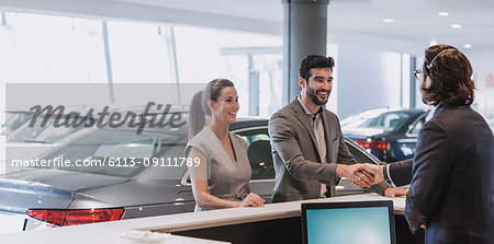 Couple arriving, greeting receptionist and handshaking at car dealership showroom