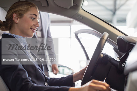 Smiling woman browsing new car, sitting in driver's seat in car dealership
