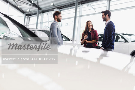 Car salesman talking to couple customers in car dealership showroom