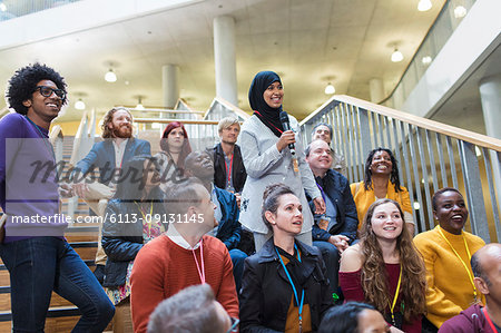 Smiling woman in hijab talking with microphone in conference audience