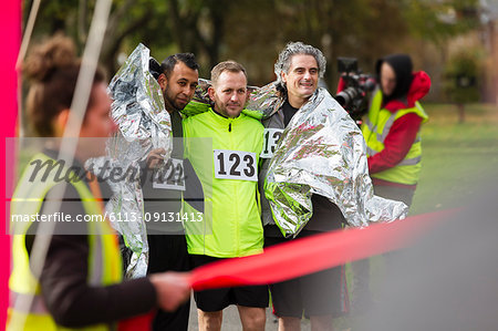 Male marathon runners wrapped in thermal blanket at finish line