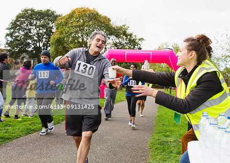 Volunteer giving water to runner at charity run in park