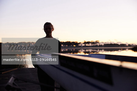 Silhouette of female rower lifting scull on sunrise lakeside dock