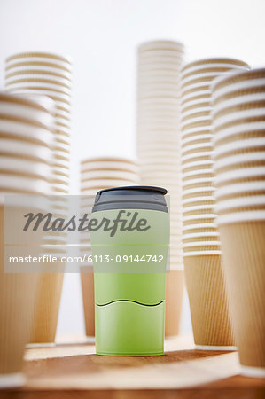 Green insulated drink container surrounded by disposable coffee cups