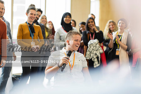 Conference audience clapping for smiling female speaker with microphone