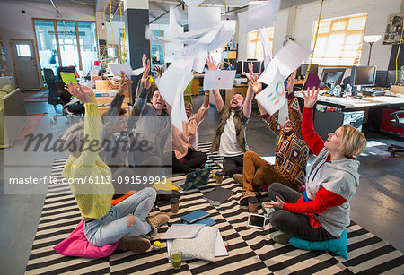 Playful, enthusiastic creative business team throwing paperwork overhead in open plan office