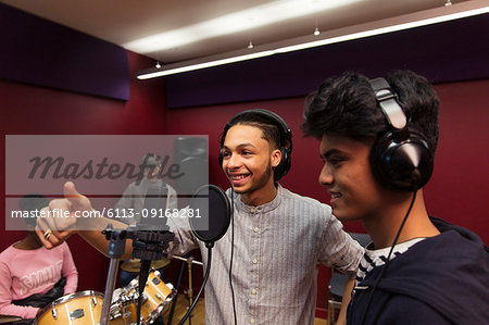 Smiling teenage musicians recording music, singing in sound booth