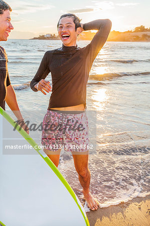 Male surfers laughing on sunny ocean beach