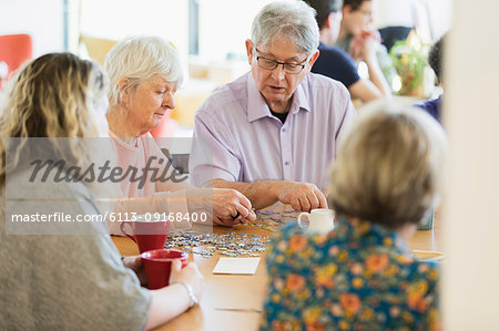 Senior friends assembling jigsaw puzzle and drinking tea at table in community center