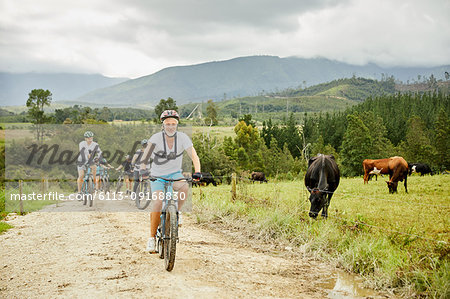 Man mountain biking with friends on rural dirt road along cow pasture